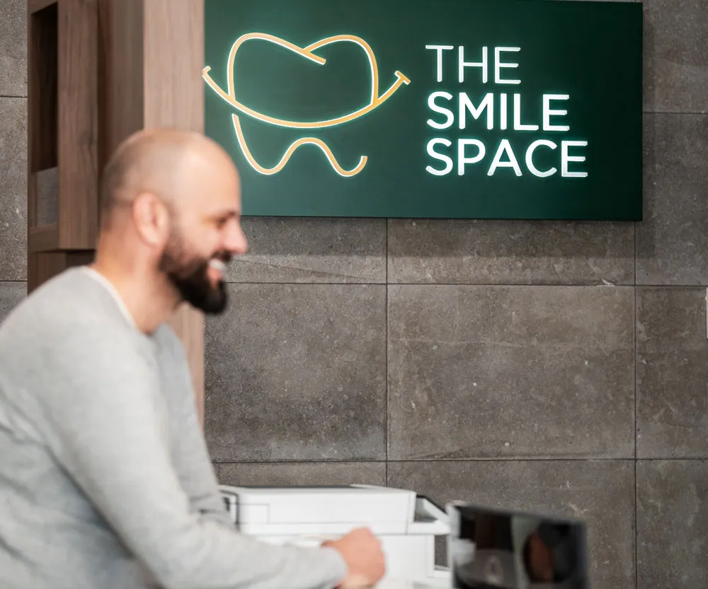 A dentist at The Smile Space reception, beneath the practice sign