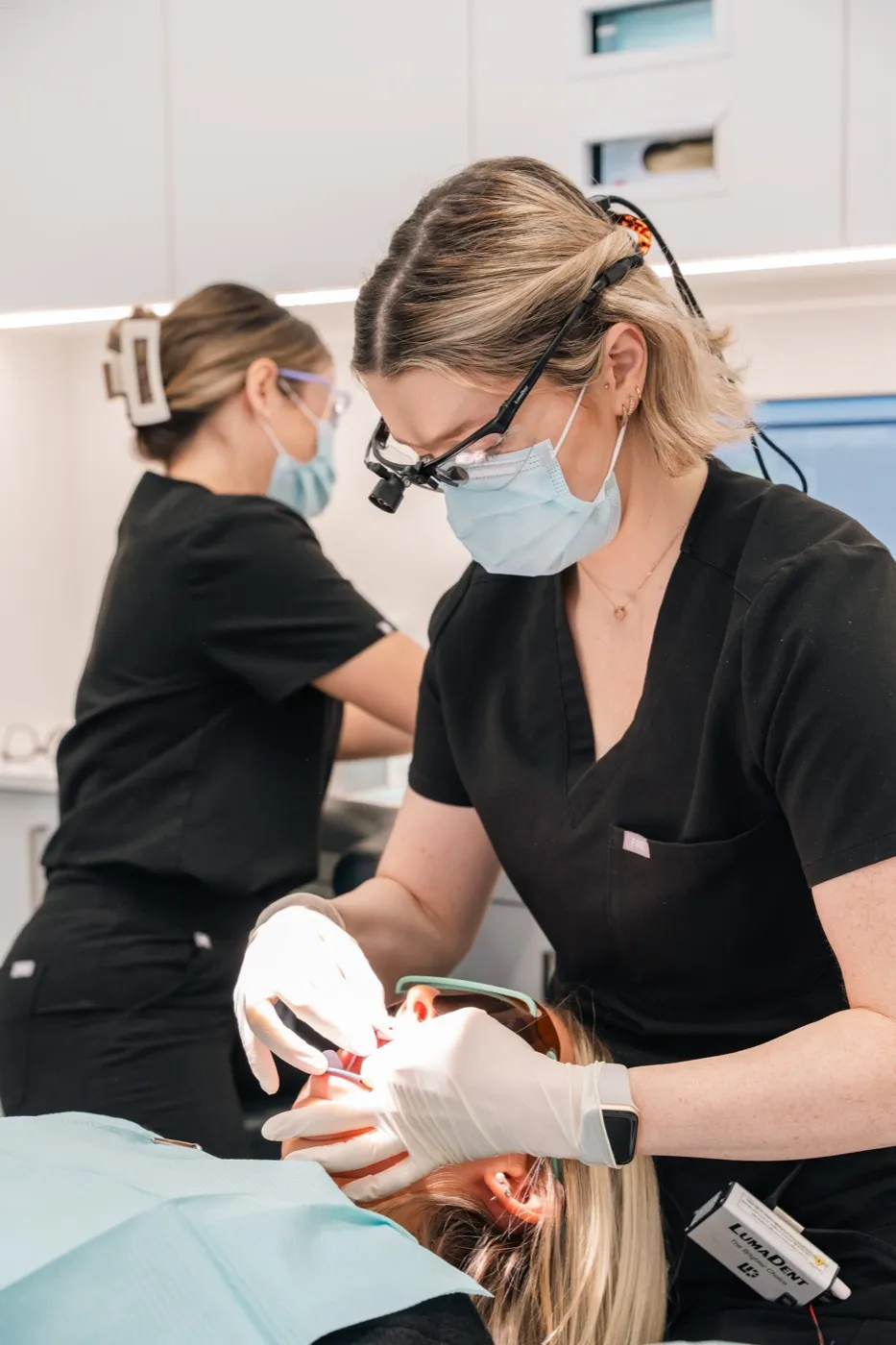 Two dental professionals in black scrubs treating a patient