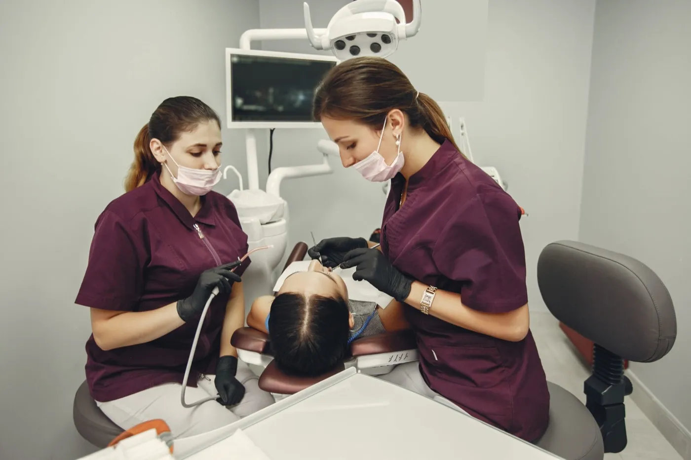 Two dental professionals in maroon scrubs treating a patient