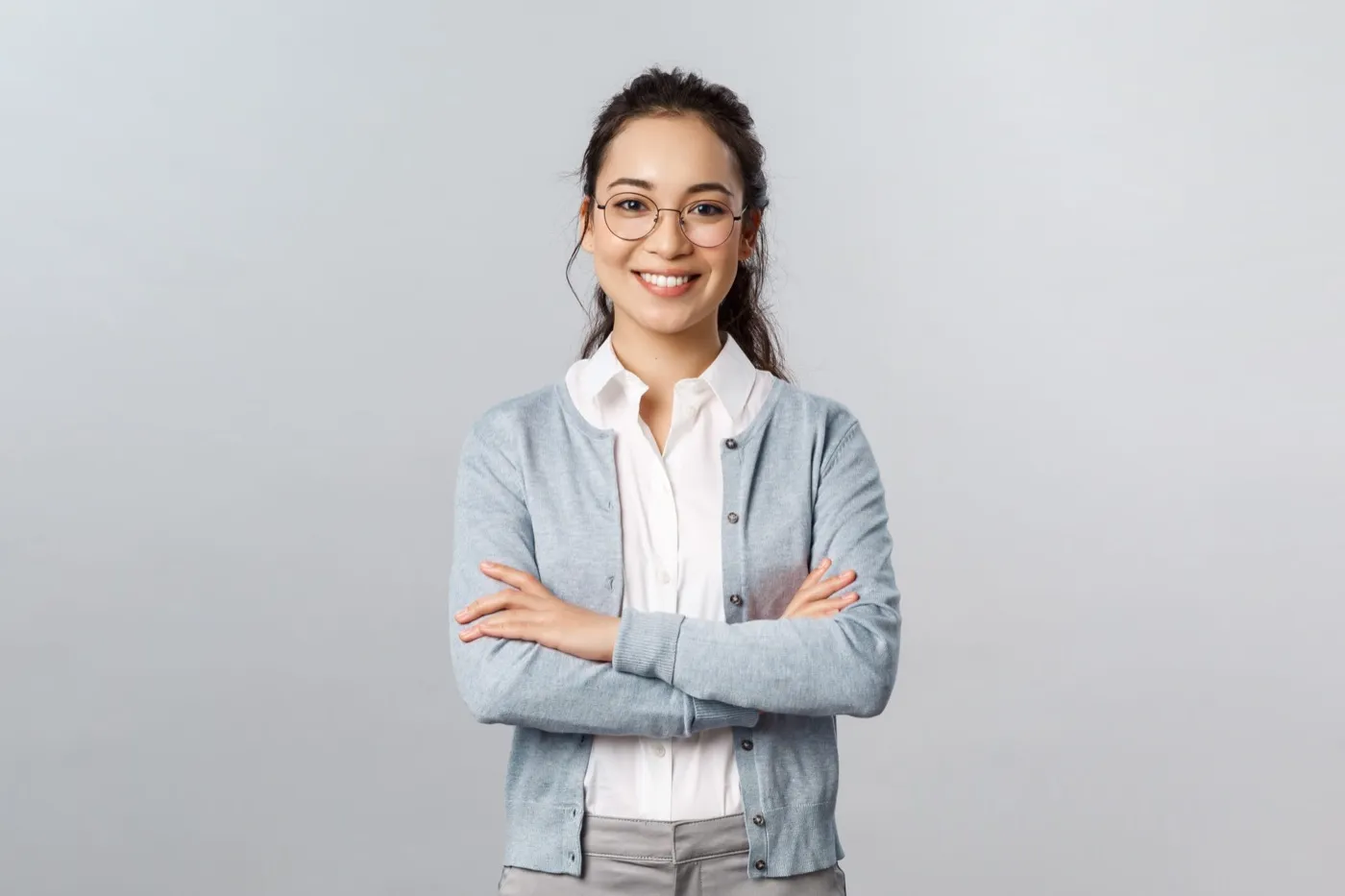 A smiling woman in glasses and a grey cardigan with her arms folded
