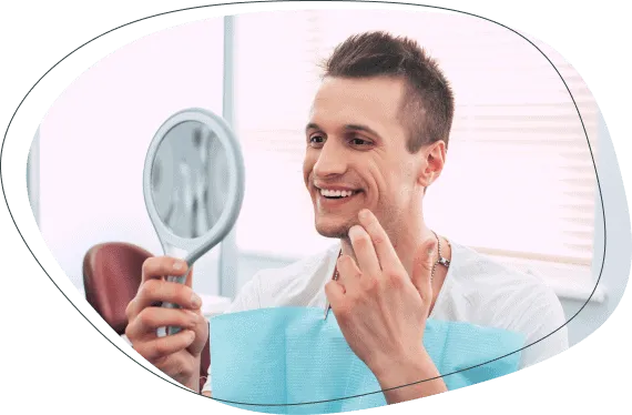 A smiling man looking at his teeth in a hand mirror