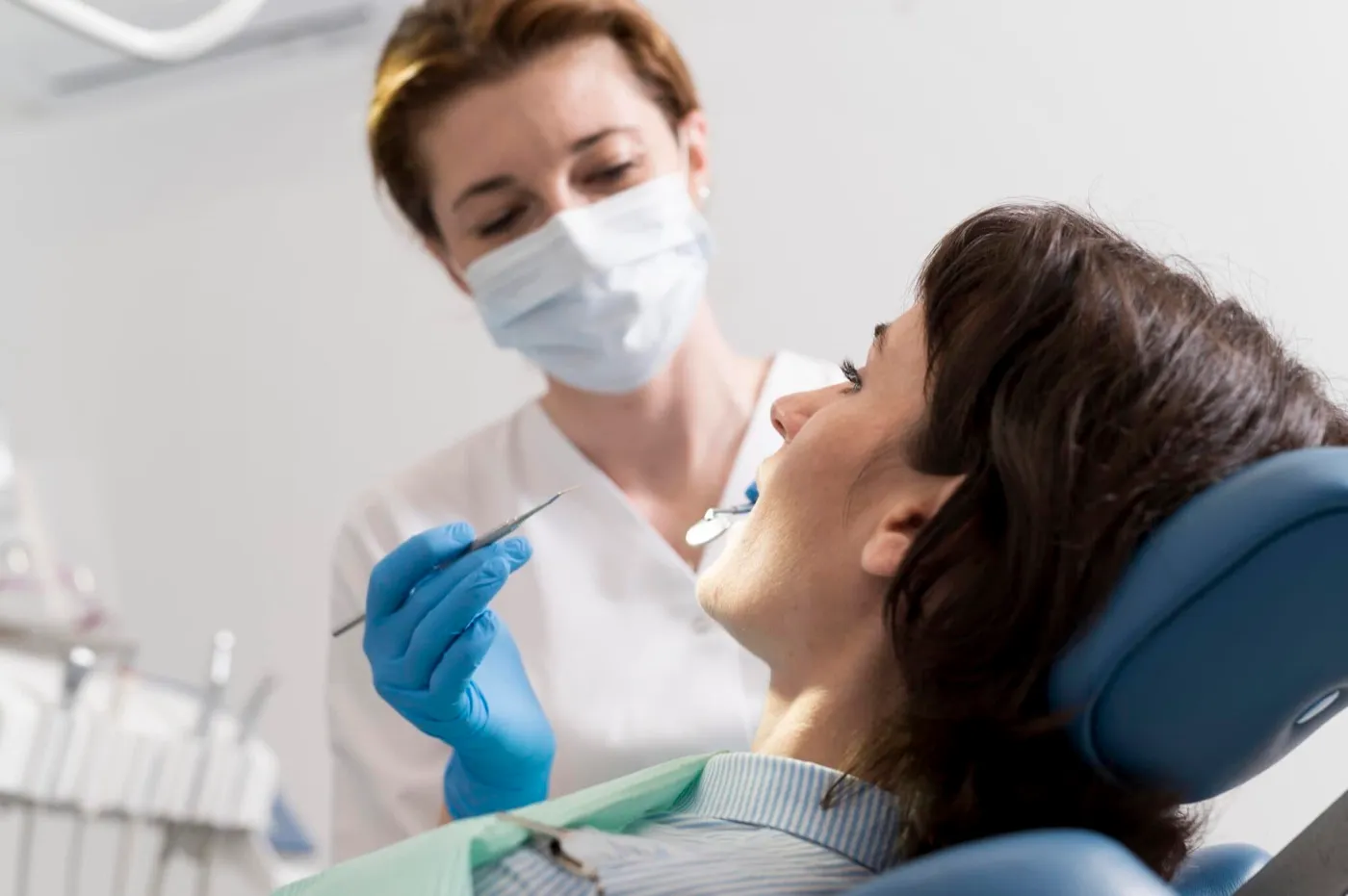 A dentist in a mask examining a woman's teeth