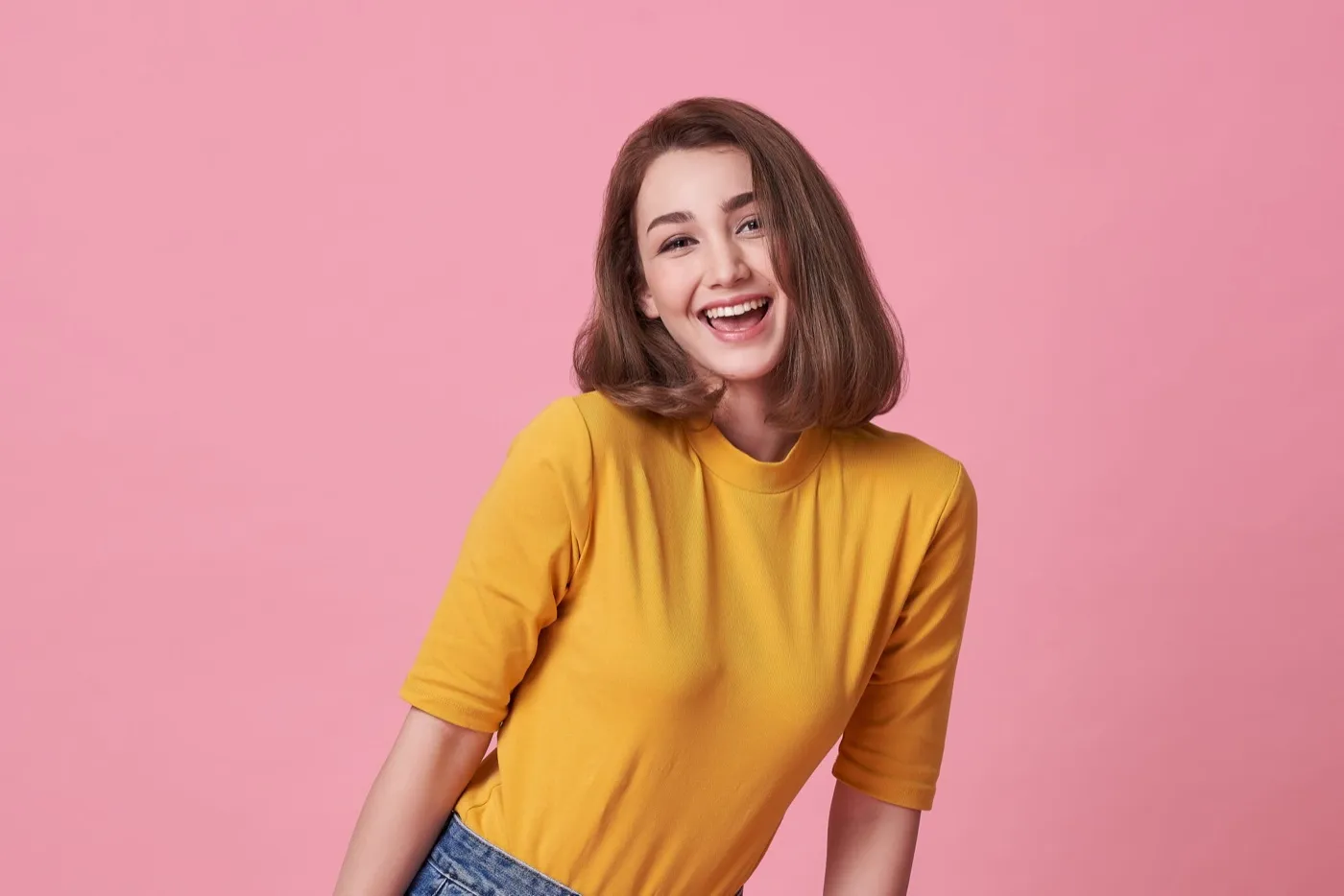 A smiling woman in a yellow top against a pink background