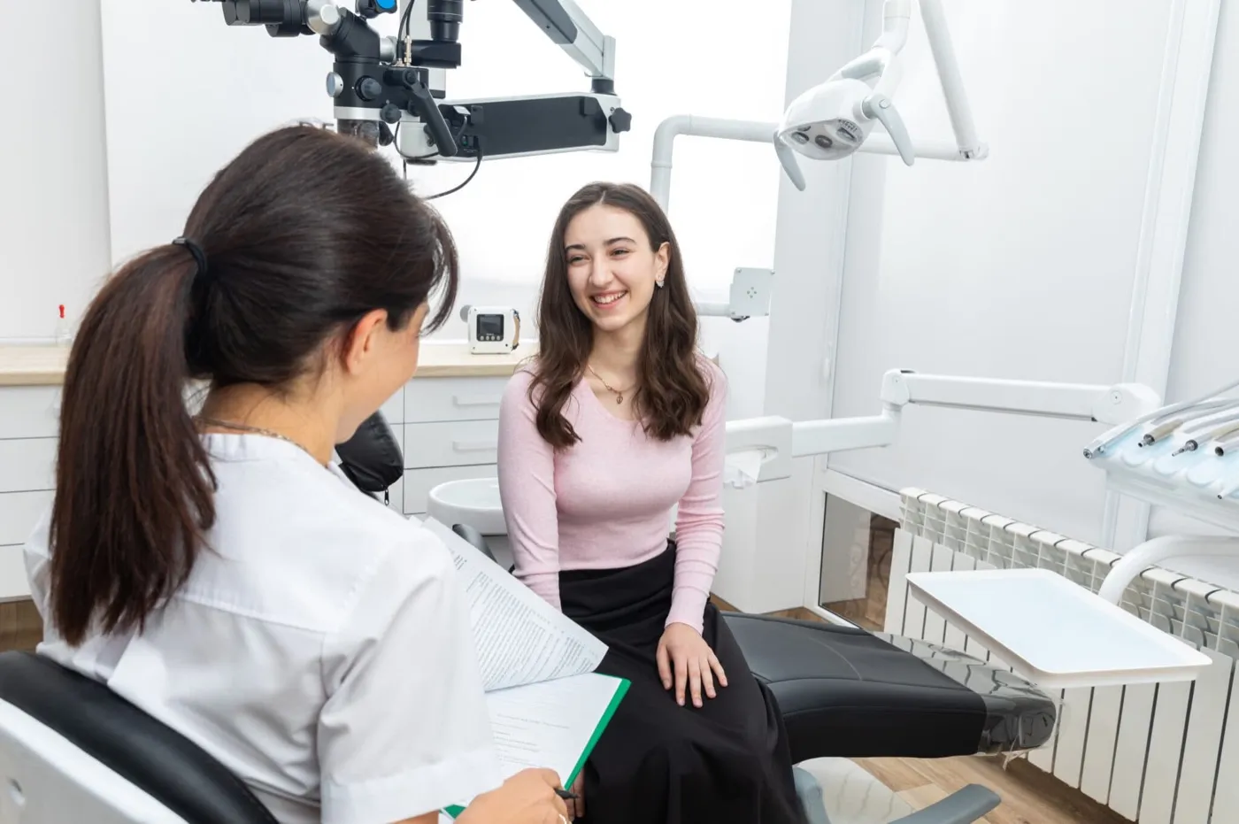 A dentist taking notes while talking with a young woman in the dental chair