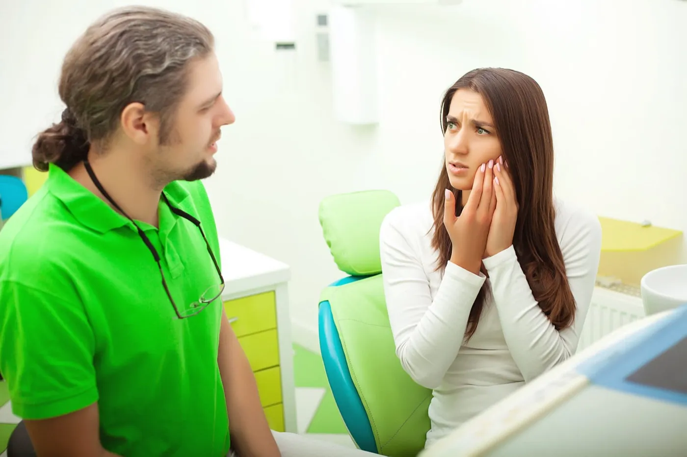 A woman holding her jaw as she talks with a dentist