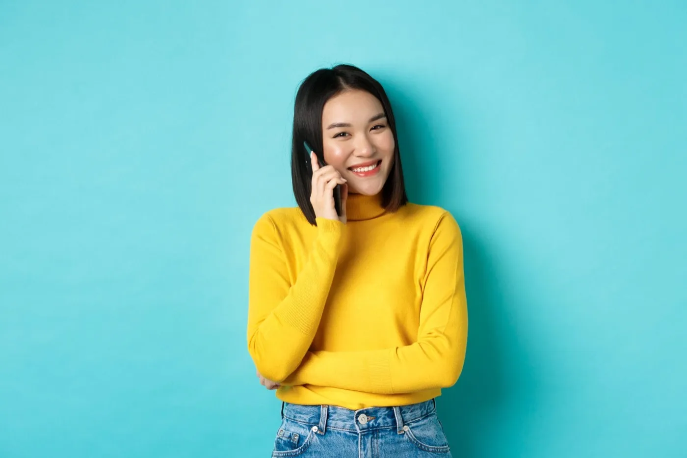 A smiling woman in a yellow jumper talking on the phone