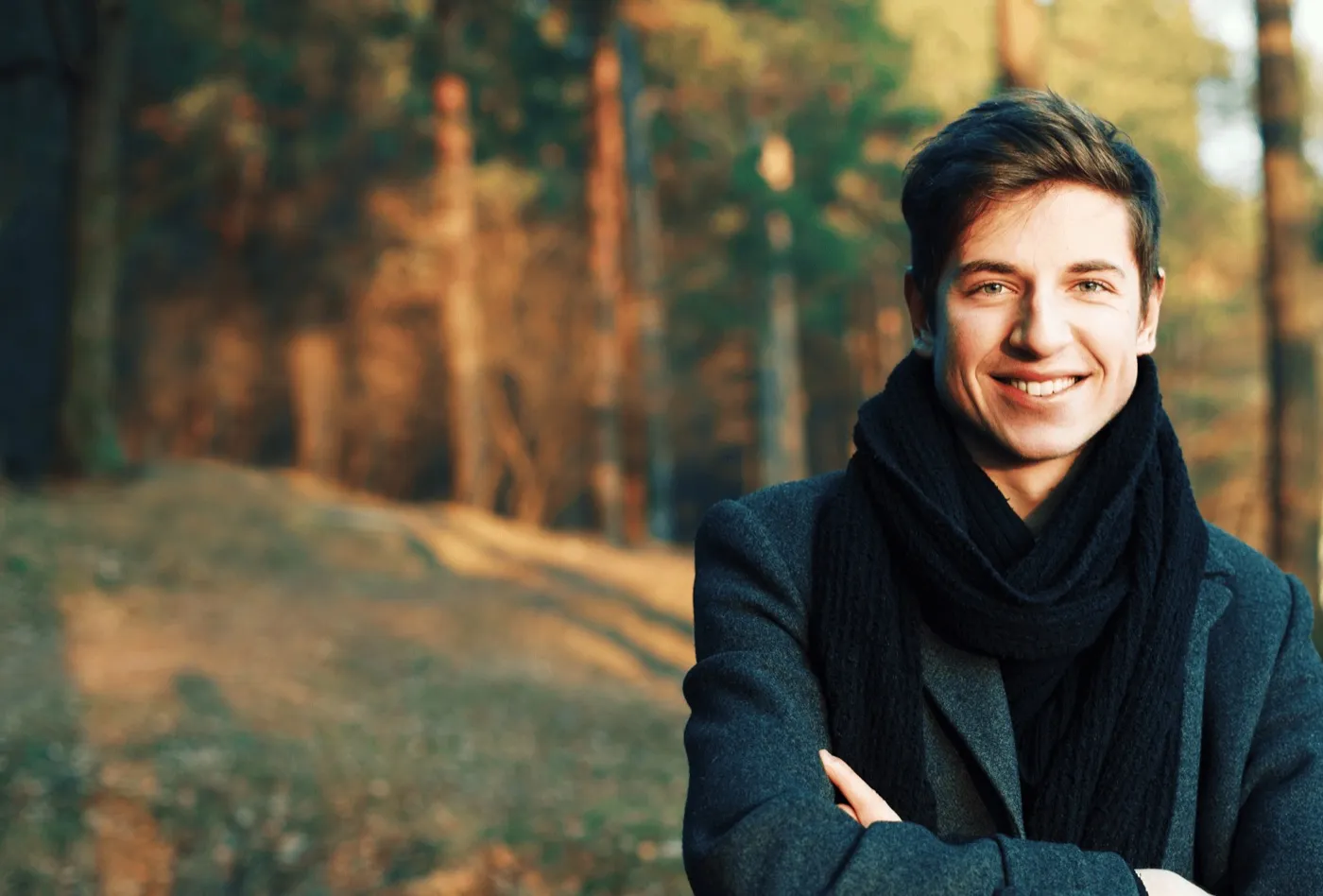 A smiling man in a dark coat and scarf outdoors