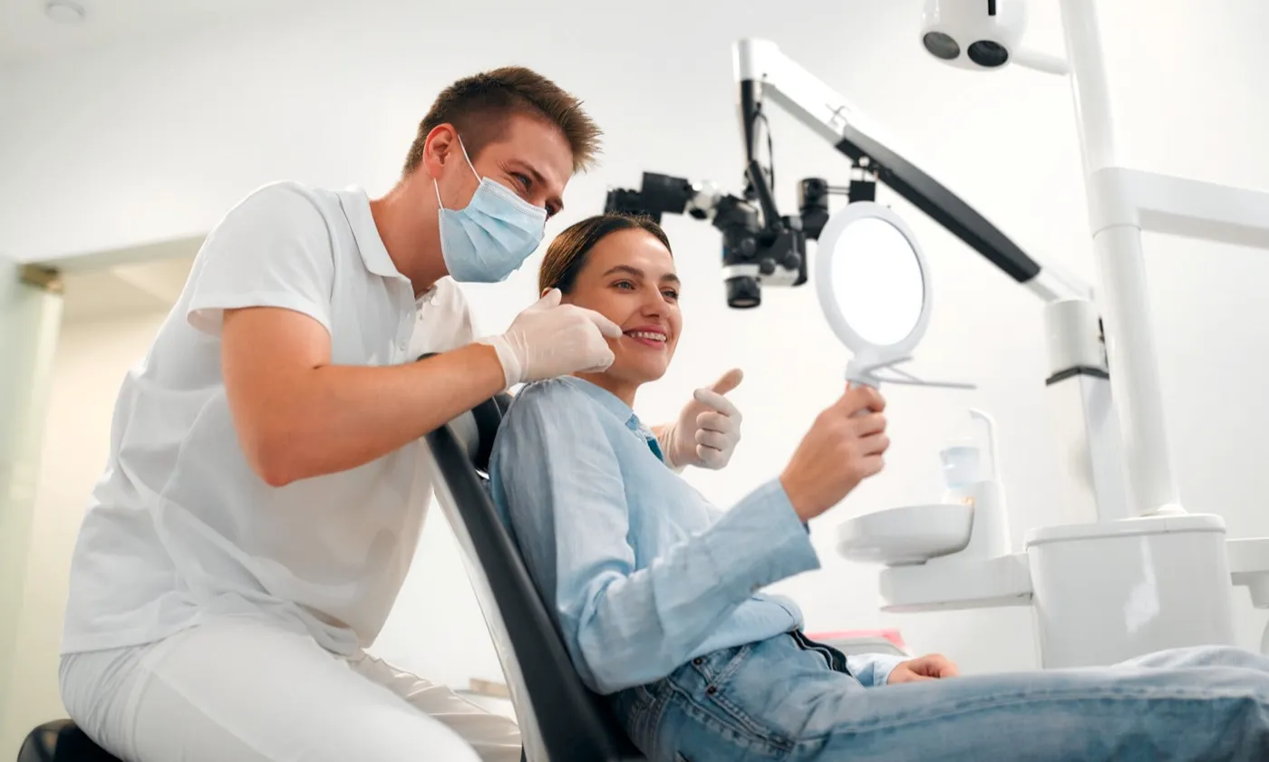 A smiling woman in the dental chair giving her dentist a thumbs up