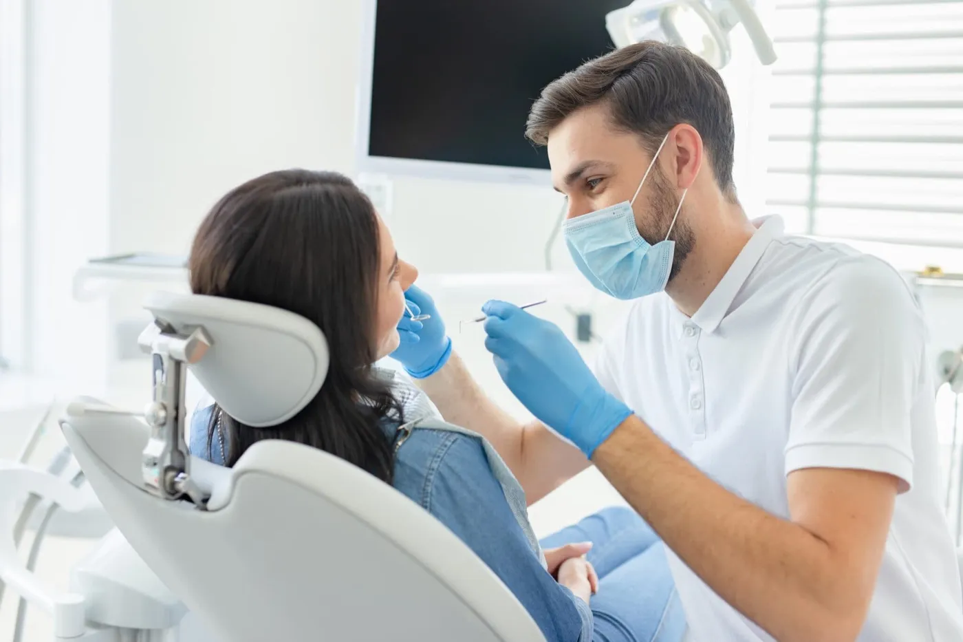 A dentist in a mask examining a woman in the dental chair
