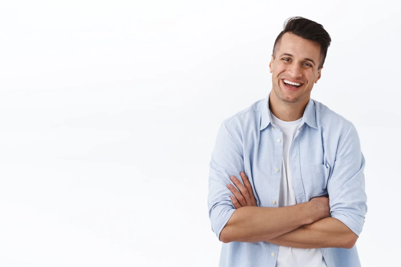 A smiling man in a light blue shirt with his arms folded