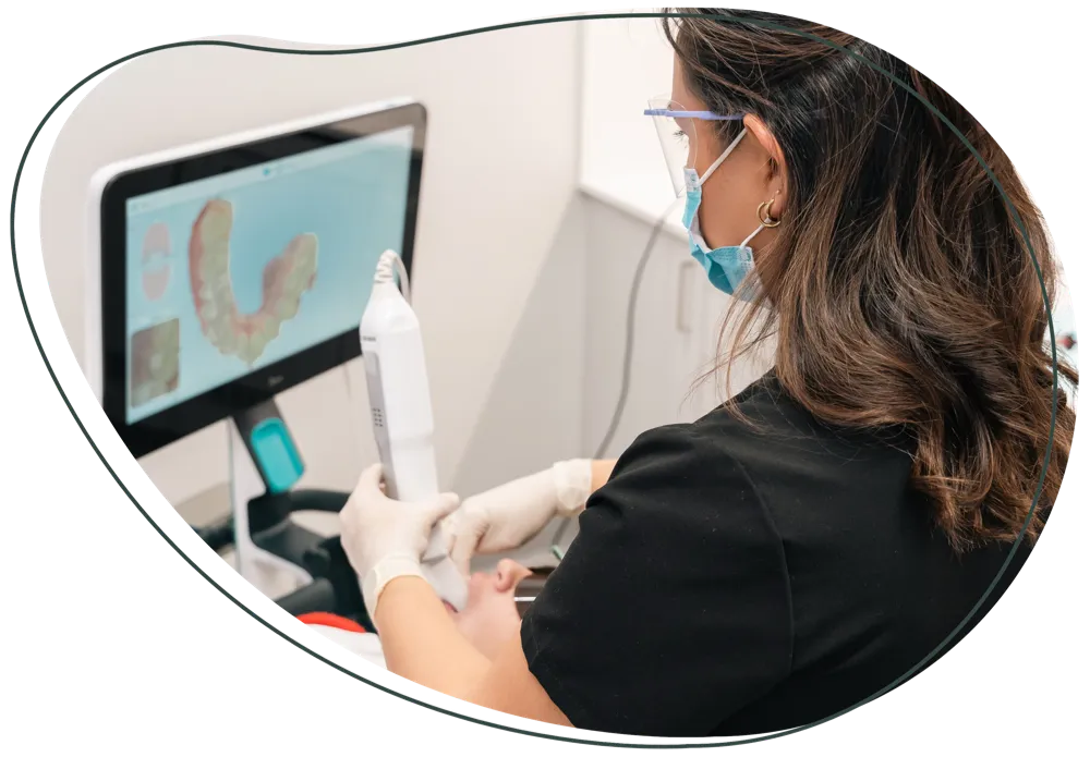 A dental team member using an intraoral scanner, with a scan of teeth on the screen