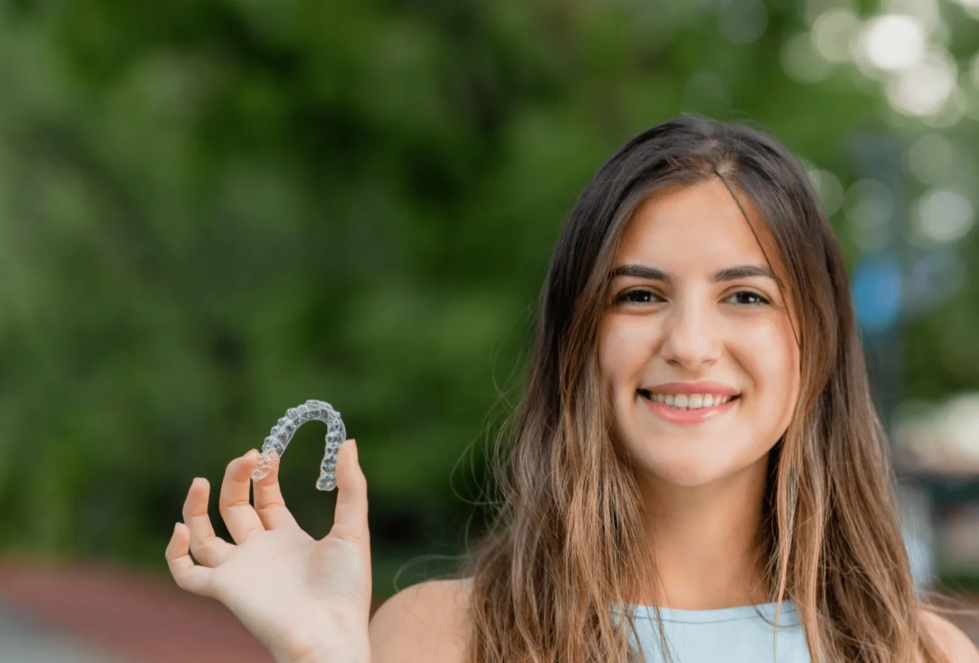 A smiling young woman holding a clear aligner