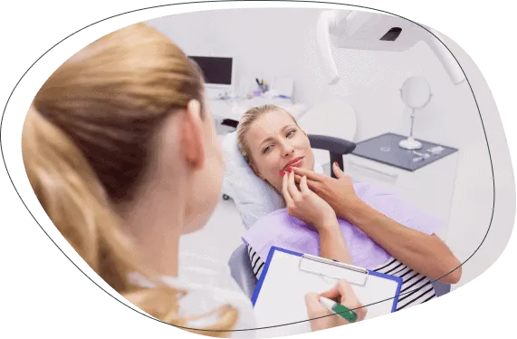 A woman in the chair holding her jaw while a dentist takes notes