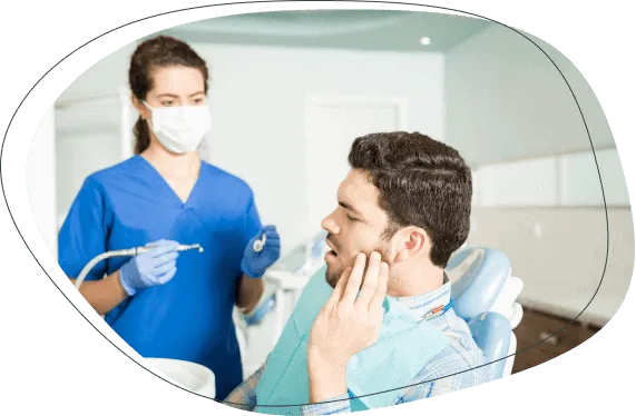 A man holding his jaw in the chair while a dentist prepares to examine him