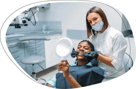 A young patient holding a hand mirror while a dentist examines her teeth