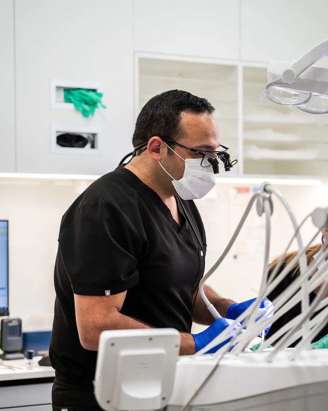 A dentist wearing a mask and magnifying loupes treating a patient